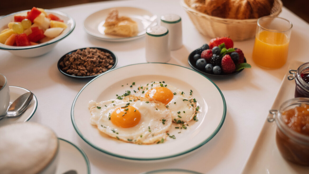 Ein Frühstückstisch mit Spiegeleiern, Obst, Gebäck, Saft und Beeren. (vergrößerte Ansicht)