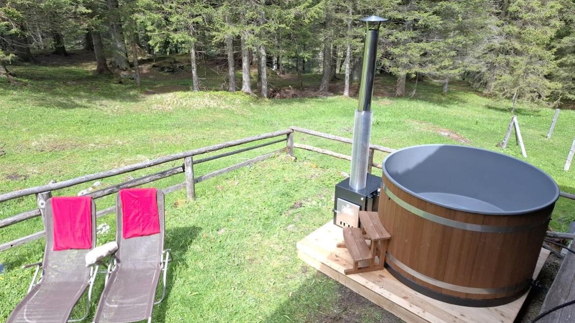 Zwei Liegestühle und ein hölzerner Whirlpool stehen auf einer Wiese in der Nähe eines Waldes. (vergrößerte Ansicht)