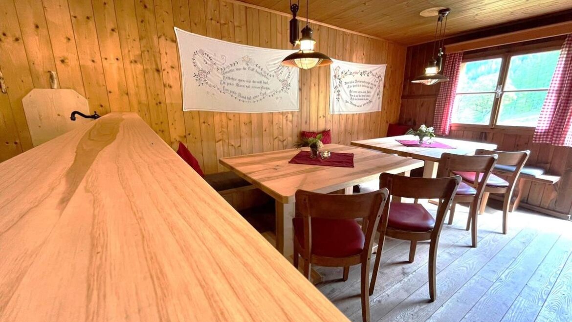 Gemütlicher hölzerner Speisesaal mit Tischen, Stühlen, Hängelampen und rot-karierten Vorhängen am Fenster. (vergrößerte Ansicht)