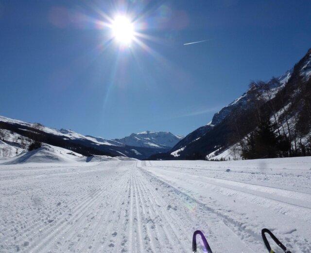 Präparierte Piste bei strahlendem Sonnenschein mit schneebedeckten Bergen und strahlend blauem Himmel im Hintergrund.