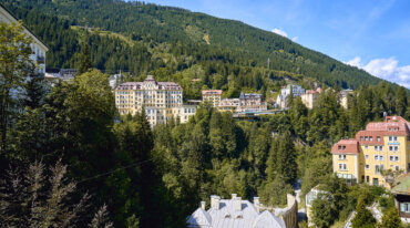 Bunte Häuser inmitten von grünen Hügeln und Bäumen unter blauem Himmel - ein Almsommer im TV-Bergtraum.