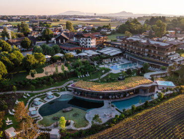 Luftaufnahme eines Luxusresorts mit Pools, Gärten und nahe gelegenen Häusern in einer ländlichen Landschaft bei Sonnenuntergang.