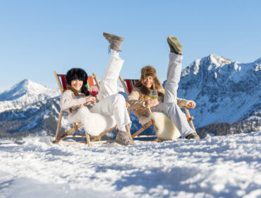 Winter Chillout im Liegestuhl, (c) SalzburgerLand Tourismus, Hansi Heckmair Zwei Frauen genießen ein Winterchillout auf Liegestühlen im Schnee, Getränke in der Hand, die Berge im Rücken.