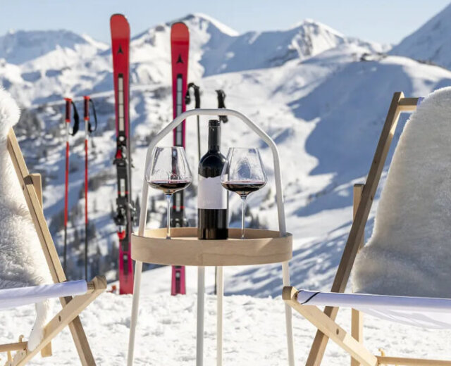Zwei Loungesessel mit Fellüberwürfen, Weingläsern und Skiern in einer verschneiten Berglandschaft im Großarltal.