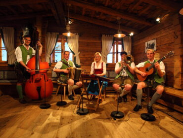 Vier Musiker und eine Musikerin in traditioneller österreichischer Kleidung spielen in der Stubn auf.