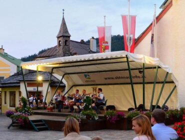 Menschen genießen ein lebhaftes Freiluftkonzert auf einem farbenfrohen europäischen Stadtplatz in der Abenddämmerung.