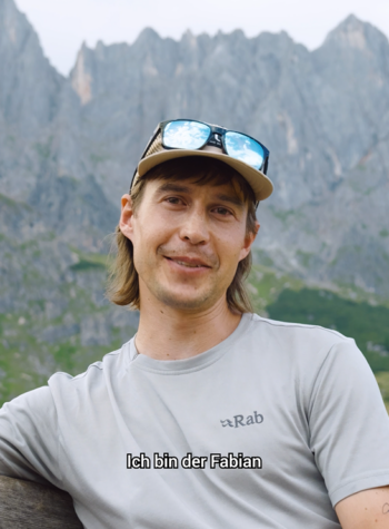 Fabian Bergner, sitzt mit einem grauen Wander T-Shirt und einer Kappe in der Region Hochkönig auf einem Salzburger Almenweg-Bankerl und erzählt von seiner Leidenschaft dem Weitwandern am Salzburger Almenweg.