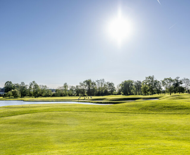 Ein sonniger Tag auf einem Golfplatz mit üppigem grünen Gras, einem Teich und Bäumen im Hintergrund.