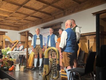 © Flachau Herbstgsang Eine Gruppe in traditioneller österreichischer Tracht musiziert auf der Bühne mit verschiedenen Instrumenten und rustikaler Dekoration.