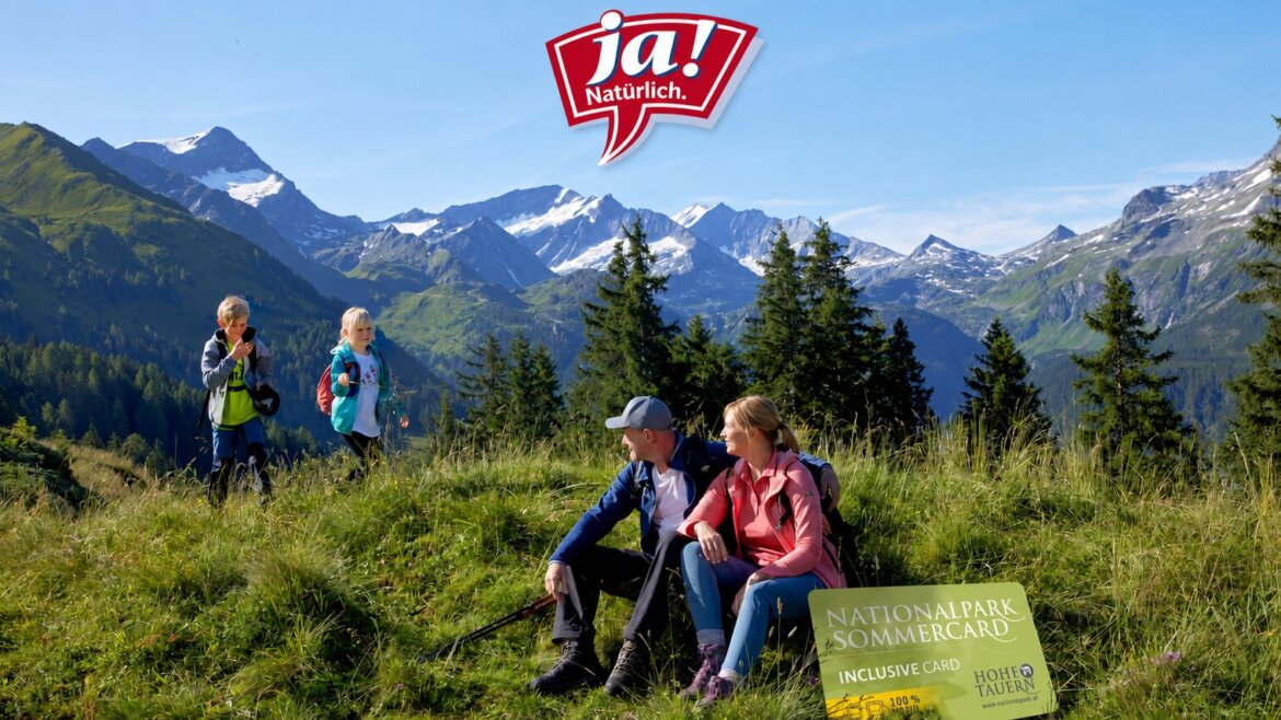 Eine Familie wandert in den grünen Bergen mit schneebedeckten Gipfeln und sitzt in der Nähe eines Schildes für den Nationalpark Sommercard. (vergrößerte Ansicht)