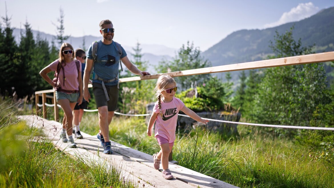 © Dorfgasteiner Bergbahnen AG, Malerwinkelsteig Eine dreiköpfige Familie wandert an einem sonnigen Tag auf dem Malerwinkelsteig in Dorfgastein. (vergrößerte Ansicht)
