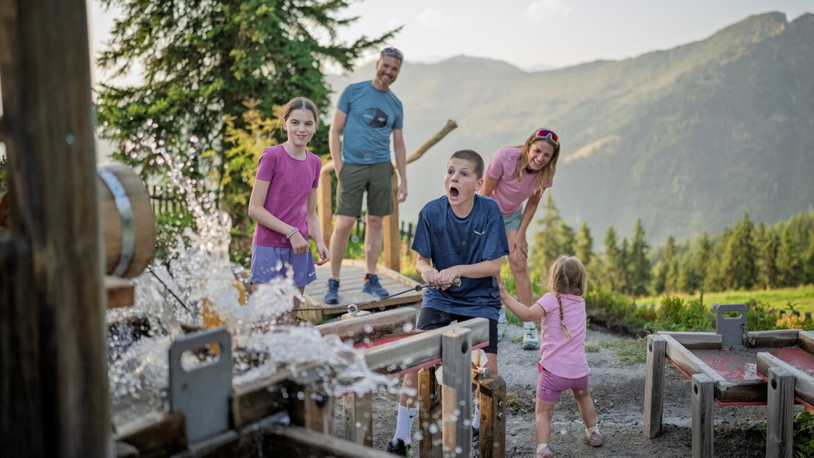 © Dorfgasteiner Bergbahnen AG, Wasserspielplatz Eine Familie, die draußen in am Wasserspielplatz am Fulseck in Dorfgastein spielt; die Kinder lachen und planschen. (vergrößerte Ansicht)