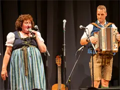 (c) Renate Maier. Gstanzl-singa Gem.Hallwang Eine Frau singt und ein Mann spielt Akkordeon auf der Bühne; beide tragen traditionelle österreichische Tracht.