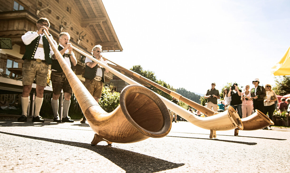 © SalzburgerLand Tourismus, Markus Berger, Bauernherbst Vier Menschen, die bei einem Festival im Freien Alphorn spielen, im Hintergrund eine Menschenmenge und ein Gebäude. (vergrößerte Ansicht)