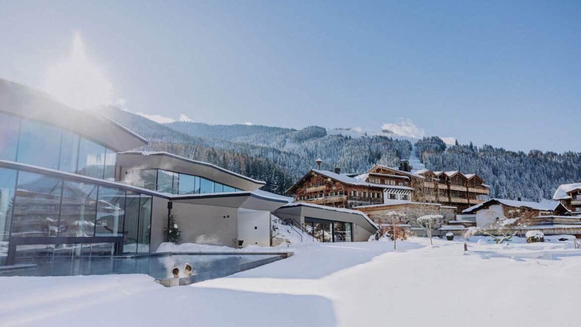 Infinity Pool Heaven Spa im Puradies © @thecreatingclick, Creating Click OG Moderne Gebäude und Holzhütten, umgeben von Schnee, mit Bergen und strahlend blauem Himmel im Hintergrund. (vergrößerte Ansicht)