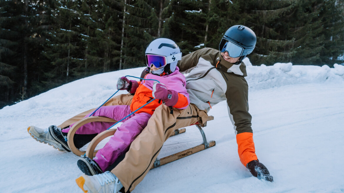 flachau winter tobogganing (c) Flachau Tourismus Adult and child in winter gear sledging in Flachau on snowy slope with trees in the background. (Enlarged view)