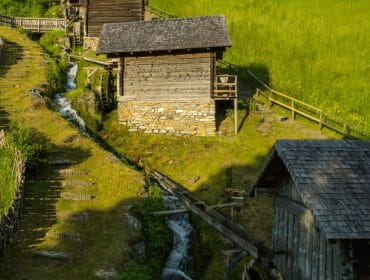 Old wooden watermills and a fence dot the green hillside near a stream in scenic Pfarrwerfen.