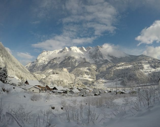 Snow-covered Werfen village with houses, snowy trees, and tall mountains under a partly cloudy blue sky.