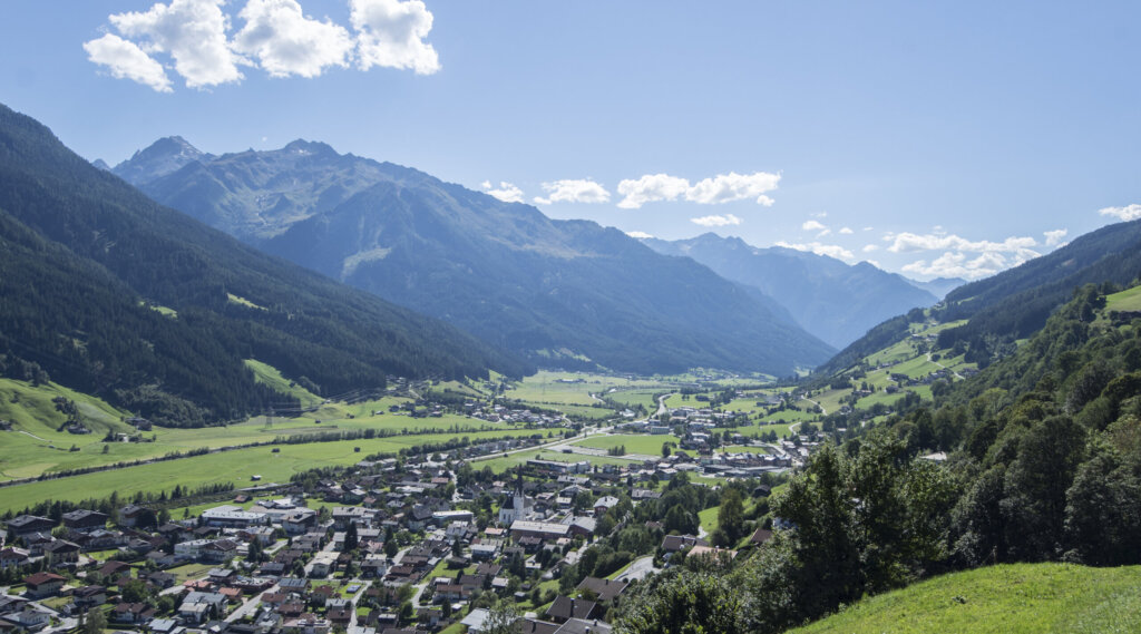Bramberg. (c) Bryan Reinhartt Bramberg is a village nestled in a green valley, surrounded by mountains under a bright blue sky with scattered clouds. (Enlarged view)