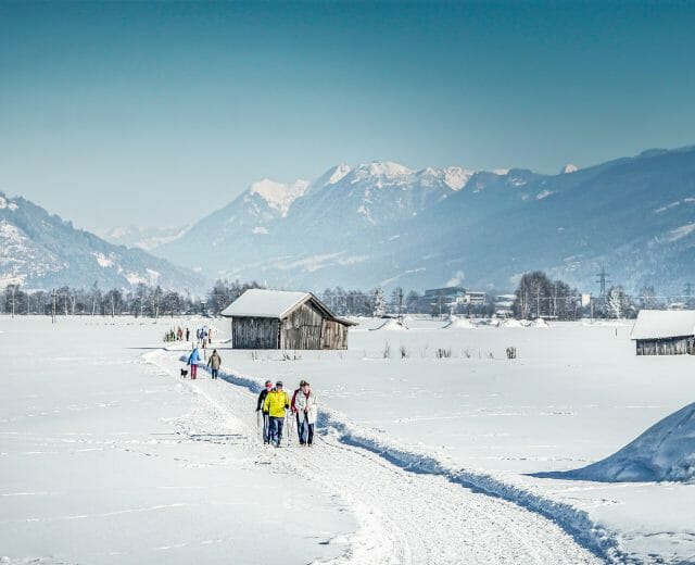 People cross-country skiing on a snowy trail near Niedernsill, with mountains and wooden cabins in the background.