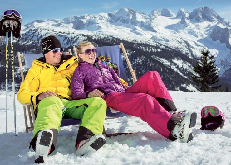 Pärchen in Skikleidung beim Entspannen im Liegestuhl vor winterlicher Kulisse