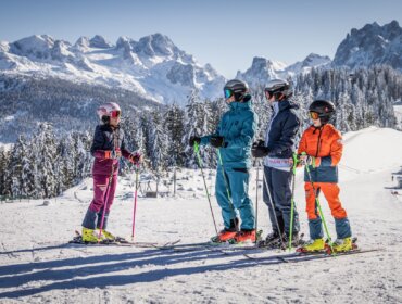 Four skiers in colourful gear stand on a snowy slope in Russbach Dachstein West with mountains and trees behind.
