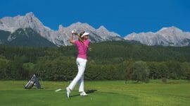 Golferin schlägt bei Kaiserwetter vor atemberaubender Bergkulisse beim Golf ab
