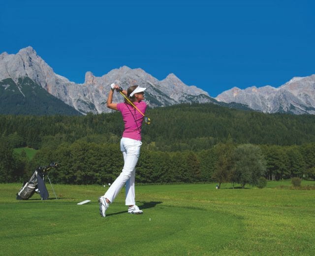 Golferin schlägt bei Kaiserwetter vor atemberaubender Bergkulisse beim Golf ab