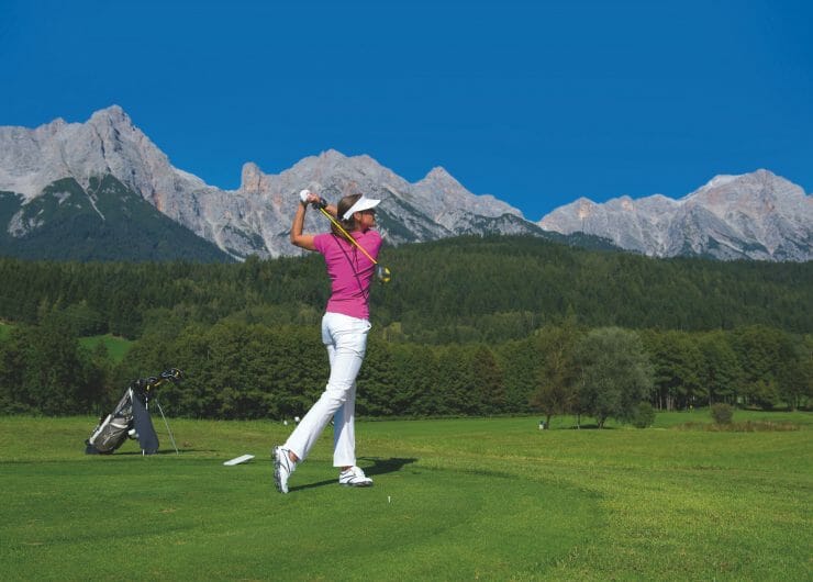 Golferin schlägt bei Kaiserwetter vor atemberaubender Bergkulisse beim Golf ab
