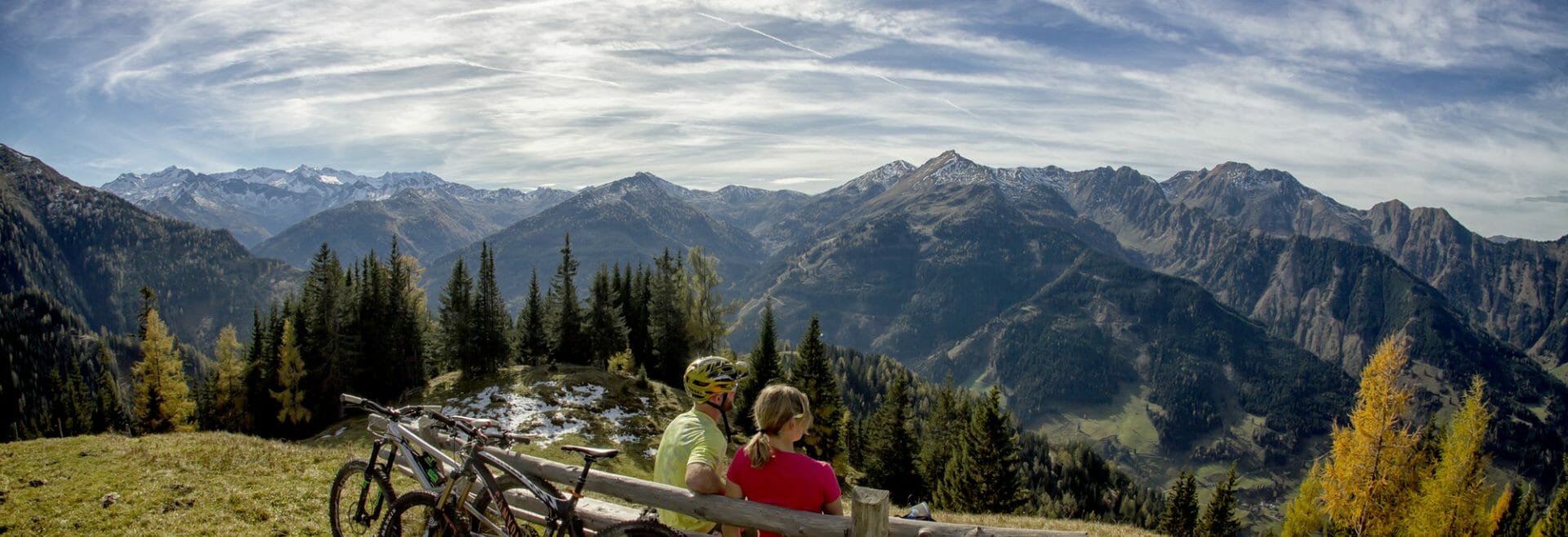 a couple sitting on a wooden bench on top of a mountain