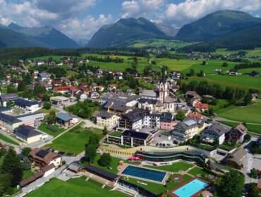 Aerial view of the village of Mariapfarr with green fields, houses, a church, and mountains in the background.