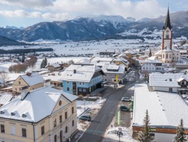 A snowy alpine village with colourful houses, a tall church spire, and mountains in the background.