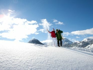 Paar steht im Tiefschnee mit Rodel im Sonnenschein
