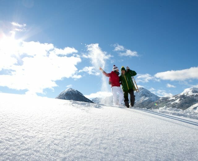 Paar steht im Tiefschnee mit Rodel im Sonnenschein