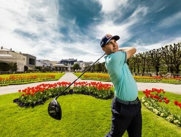A golfer practises golf swings in a garden of blooming tulips and manicured lawns under a blue sky.
