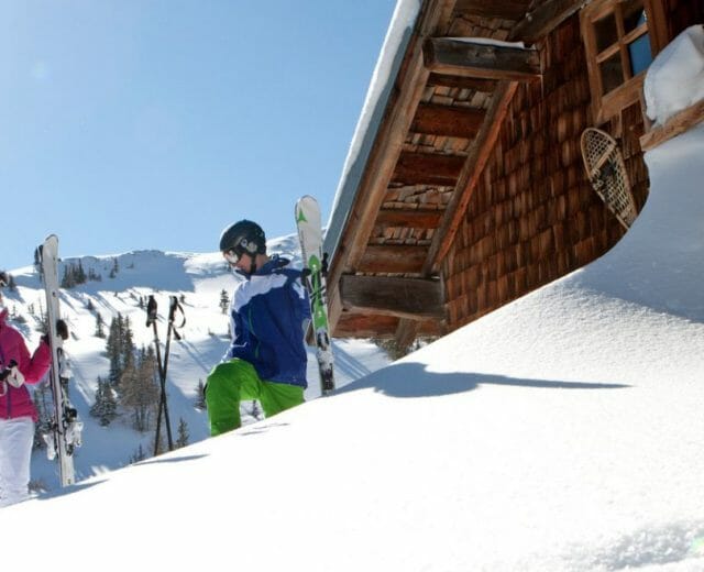 Skifahrer stehen vor einer tiefverschneiten Hütte in der Sonne