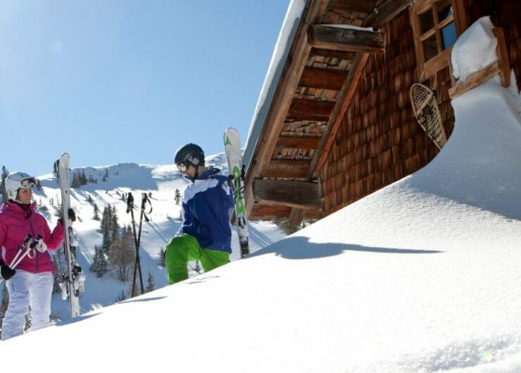 Skifahrer stehen vor einer tiefverschneiten Hütte in der Sonne