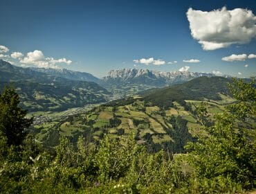 A panoramic view of a green valley with mountains in the distance under a blue sky with scattered clouds.