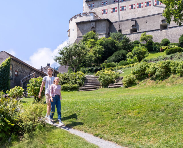 A man and child walk towards a hilltop castle in lush SalzburgerLand, perfect for exploring with a SalzburgerLand Card.