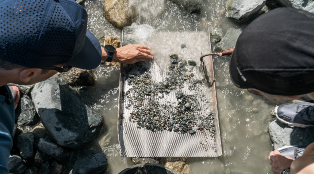 Treasure Hunt (c) Peter Maier Two people sift rocks and gravel through a metal sieve in a shallow, rocky Bramberg stream. (Enlarged view)