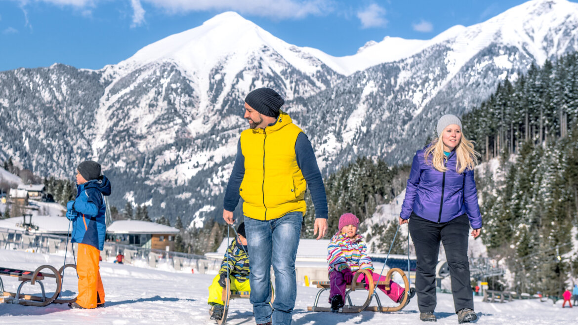 (c) Gasteinertal Tourismus GmbH, Creatina A family with children enjoys sledging in a snowy mountain landscape on a sunny winter day. (Enlarged view)