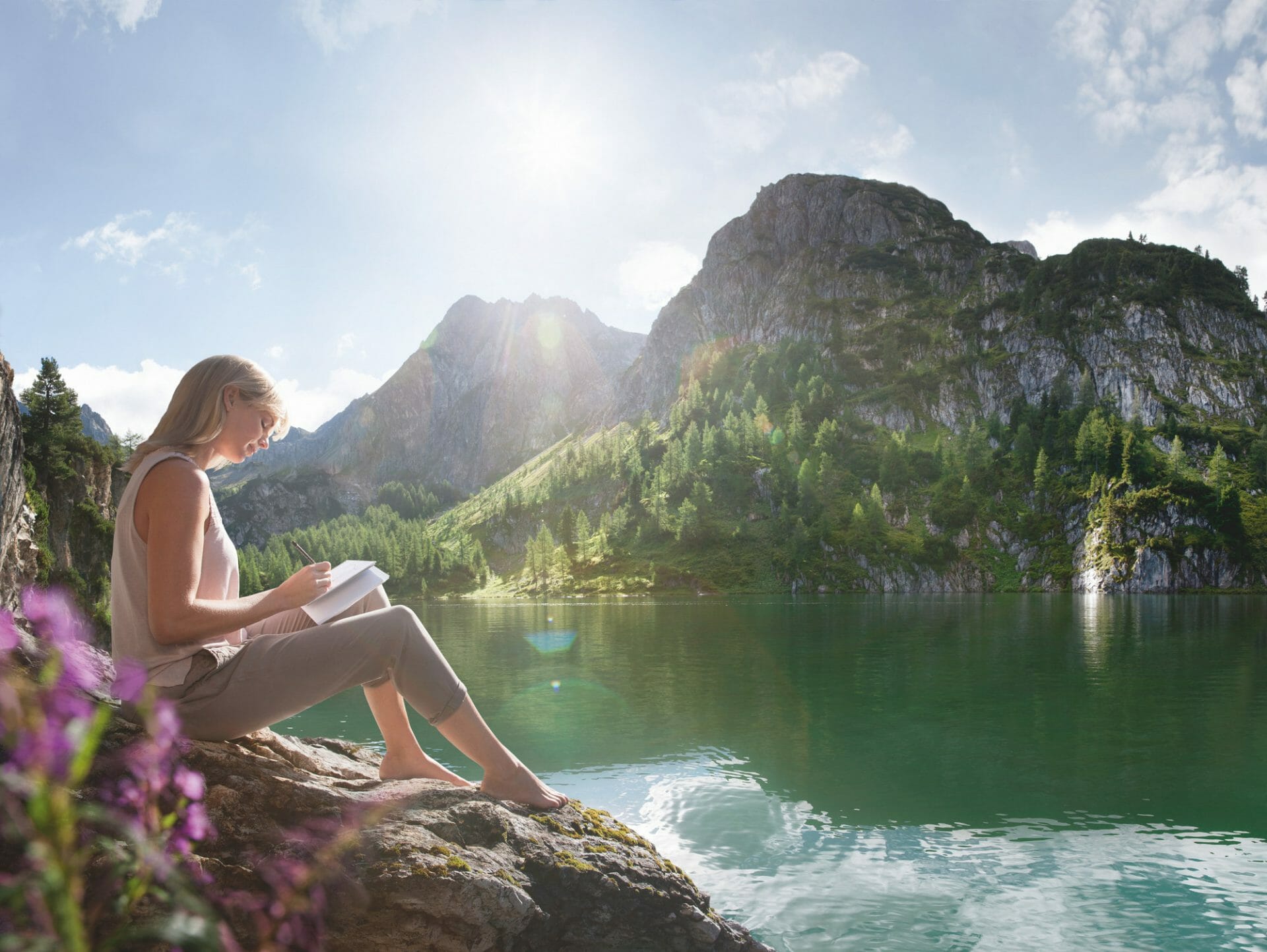 a woman reading and sitting on a rock next to water