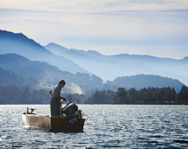 a man in a boat on the water with a mountain in the background