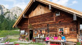A family enjoys a meal at a wooden table outside their cabin, soaking in the charm of Alpine summer events.