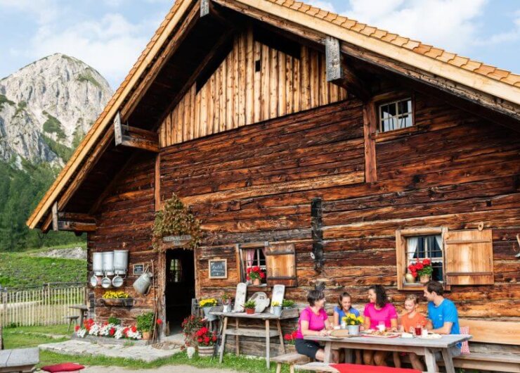 A family enjoys a meal at a wooden table outside their cabin, soaking in the charm of Alpine summer events.