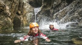 two people swimming next to a waterfall 