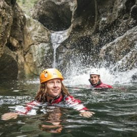 two people swimming next to a waterfall 
