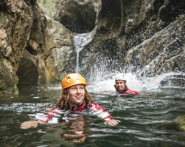 two people swimming next to a waterfall 