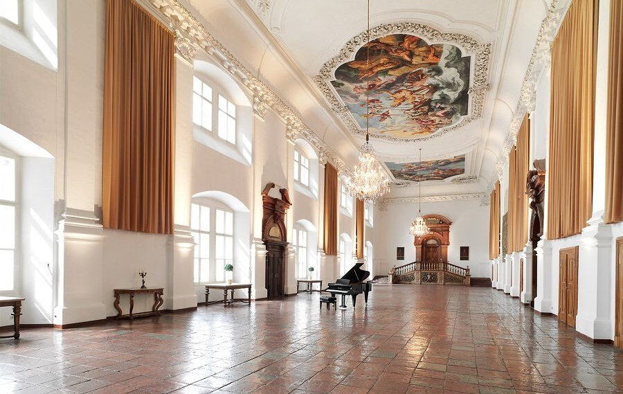 Carabinierisaal Residenz Domquartier (c) Domquatier Grand hall with chandeliers, a painted ceiling, tall windows, and a black piano for Mozart’s melodies. (Enlarged view)