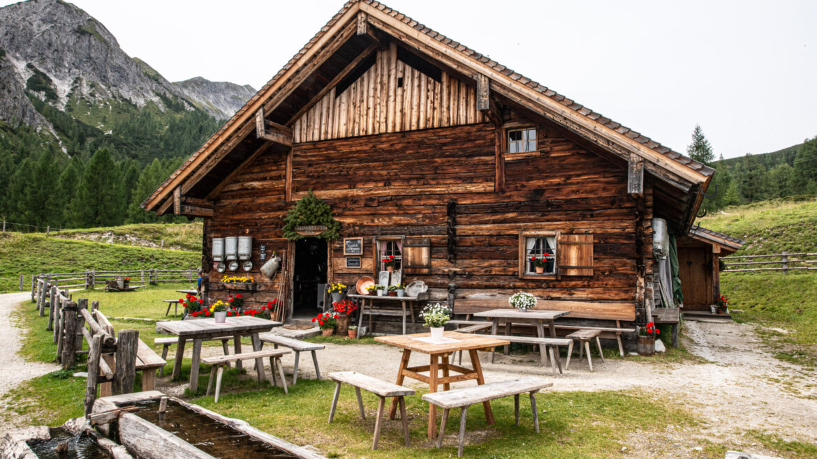 Tauernkarleitenalm (c) Untersulzberghof Tauernkarleitenalm - a rustic wooden cabin with outdoor seating, perfect for Alpine summer events amid greenery and flowers. (Enlarged view)